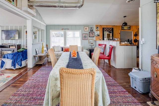 dining room with vaulted ceiling, wood walls, visible vents, and hardwood / wood-style flooring