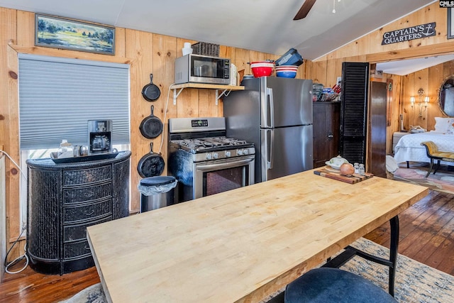 kitchen with lofted ceiling, wood walls, appliances with stainless steel finishes, and hardwood / wood-style flooring