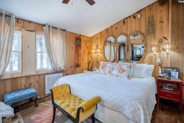 bedroom with visible vents, ceiling fan, vaulted ceiling, wooden walls, and wood finished floors