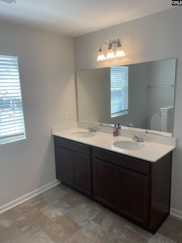 bathroom featuring toilet, a sink, baseboards, and double vanity