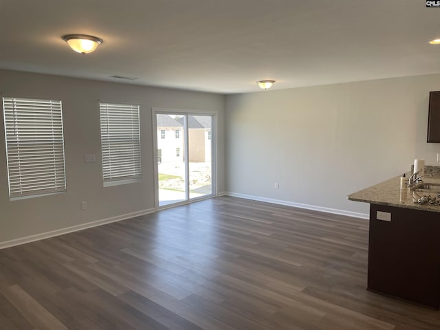 unfurnished living room with dark wood-style floors, visible vents, a sink, and baseboards