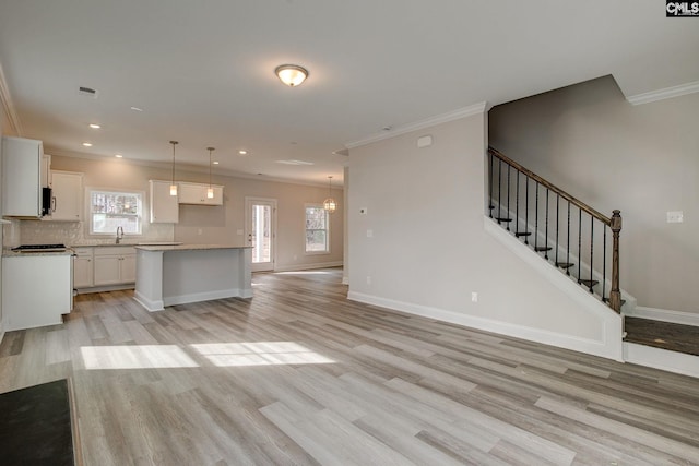 unfurnished living room featuring visible vents, light wood-style floors, a sink, baseboards, and stairs