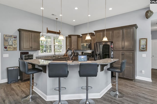 kitchen with dark wood-style floors, stainless steel appliances, light stone counters, and a kitchen island with sink