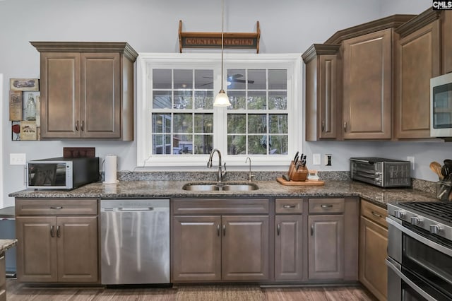 kitchen with a toaster, stainless steel appliances, wood finished floors, a sink, and dark stone counters