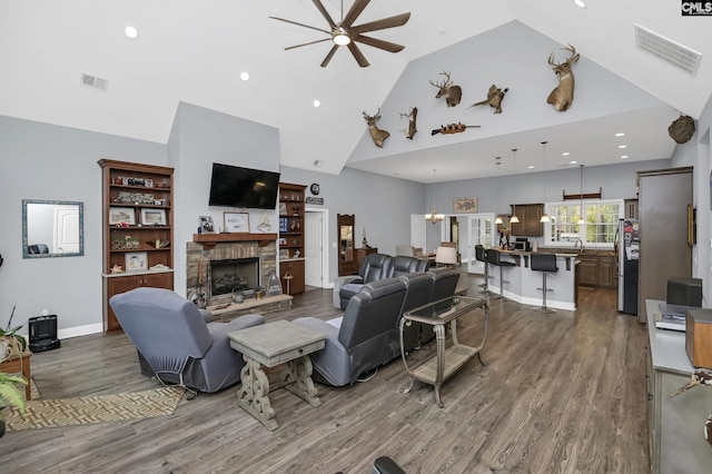 living area featuring dark wood-type flooring, visible vents, high vaulted ceiling, and a stone fireplace