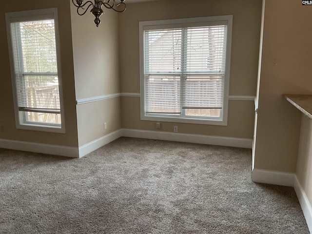 empty room featuring an inviting chandelier, baseboards, and carpet flooring