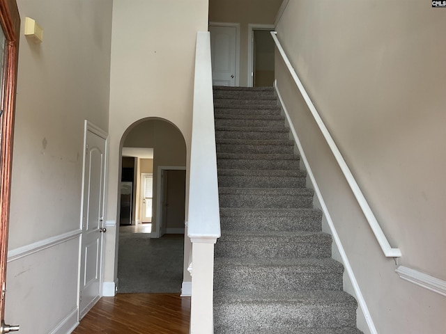 stairs featuring arched walkways, a high ceiling, wood finished floors, and baseboards