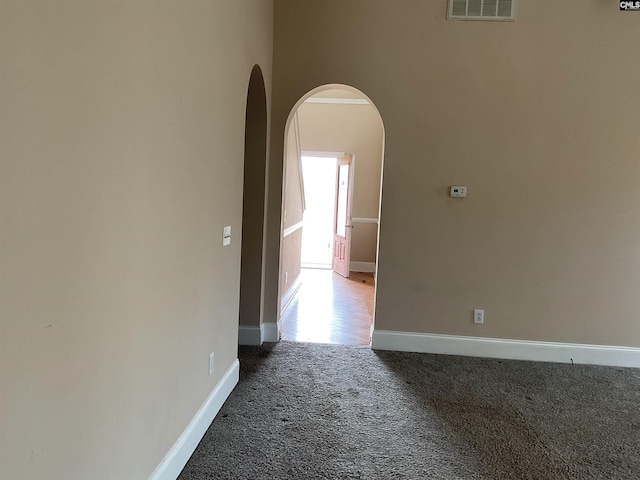 spare room featuring carpet floors, arched walkways, visible vents, and baseboards