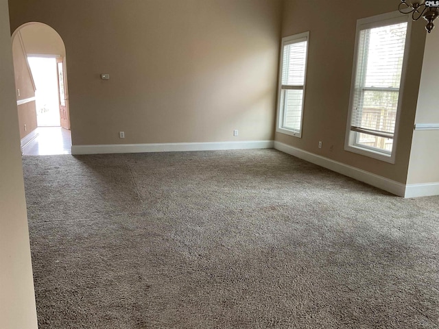 spare room featuring arched walkways, carpet, and baseboards