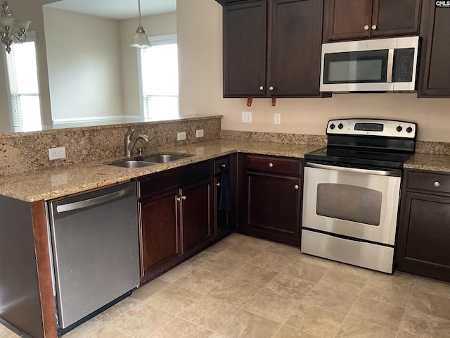 kitchen with light stone counters, stainless steel appliances, a sink, dark brown cabinets, and a peninsula