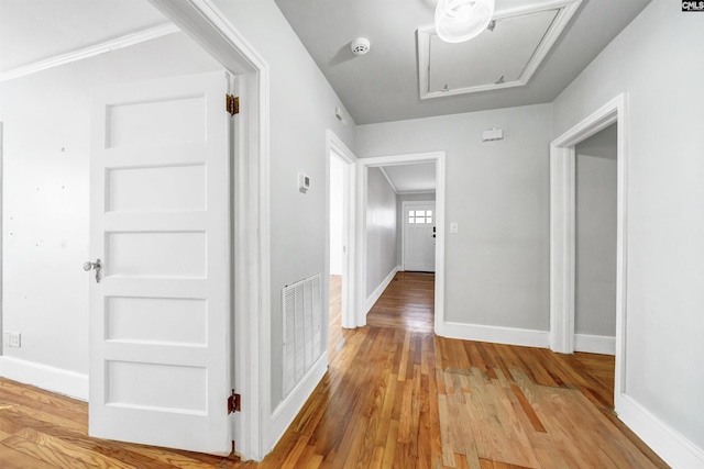 hallway with light wood finished floors, attic access, visible vents, and baseboards