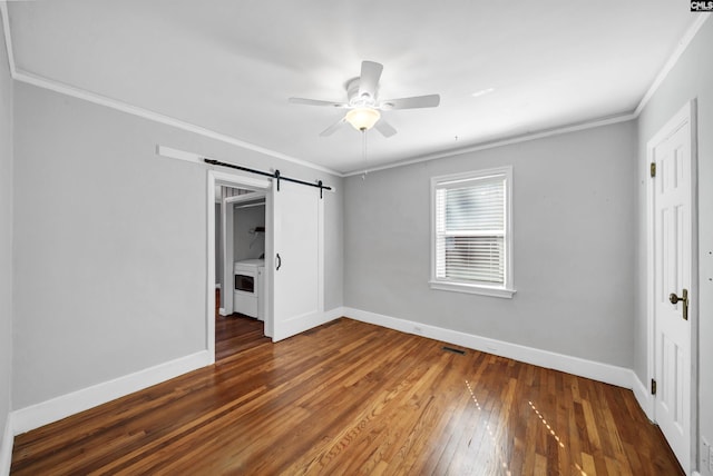 unfurnished bedroom featuring a barn door, visible vents, baseboards, hardwood / wood-style flooring, and crown molding