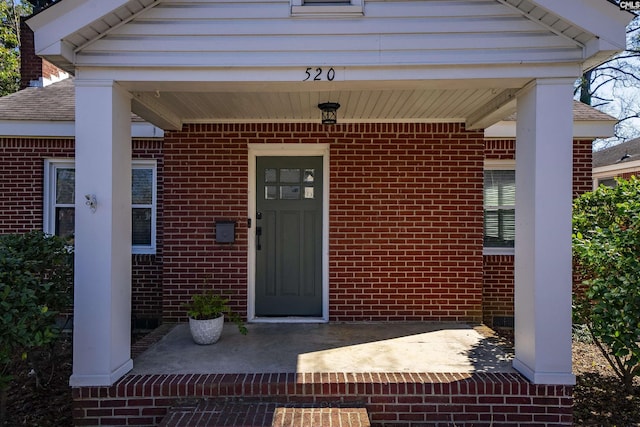 property entrance with a shingled roof and brick siding