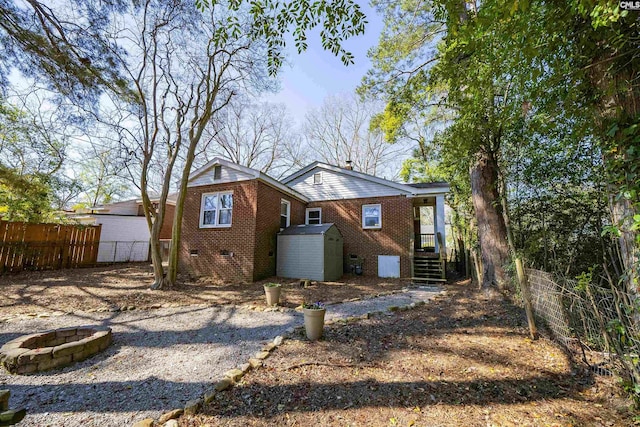 back of house featuring a storage shed, a fire pit, crawl space, fence, and brick siding