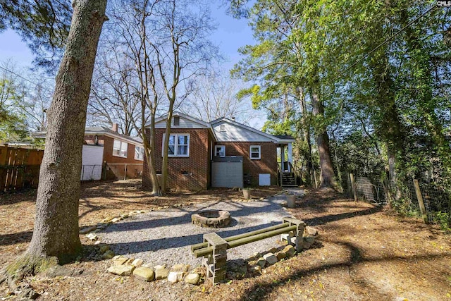 back of house with crawl space, brick siding, an outdoor fire pit, and fence