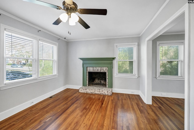 unfurnished living room featuring a brick fireplace, plenty of natural light, crown molding, and wood finished floors