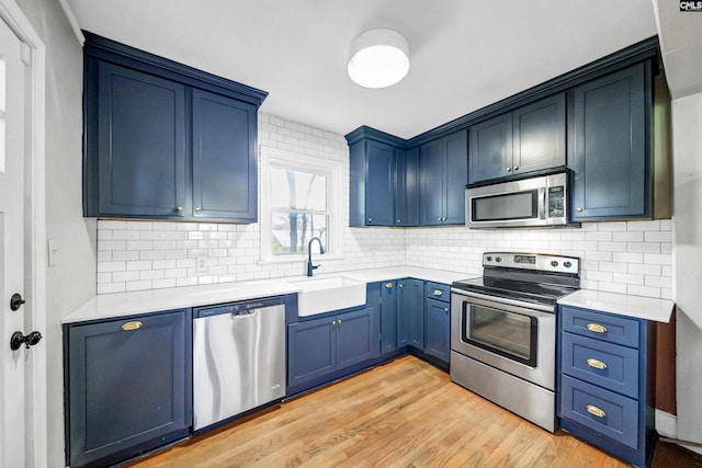 kitchen with appliances with stainless steel finishes, blue cabinets, light countertops, light wood-type flooring, and a sink