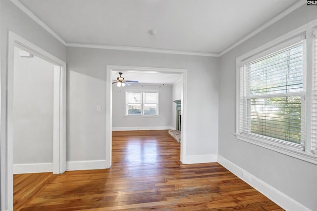 spare room with ornamental molding, a fireplace with raised hearth, baseboards, and wood finished floors