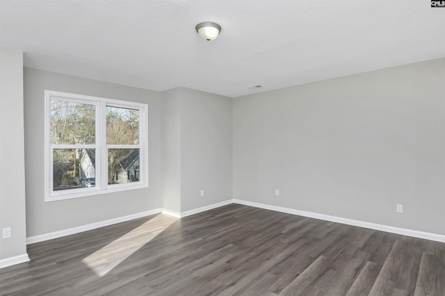 spare room featuring dark wood-style flooring, visible vents, and baseboards