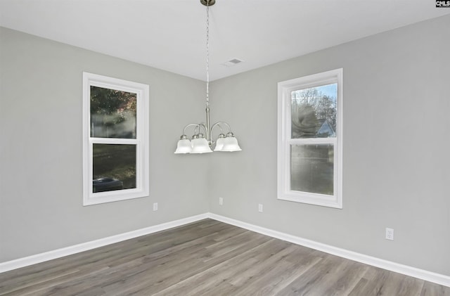 spare room with an inviting chandelier, baseboards, and wood finished floors