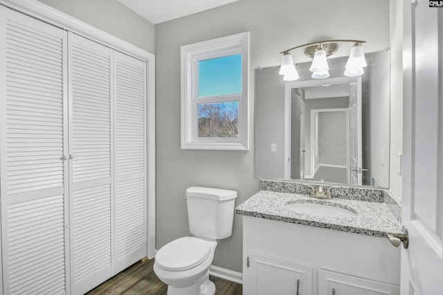 bathroom featuring a closet, toilet, vanity, wood finished floors, and baseboards