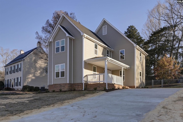 view of side of property featuring covered porch, central AC, and fence