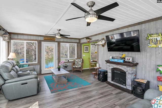 living area featuring a ceiling fan, a stone fireplace, wooden walls, and wood finished floors