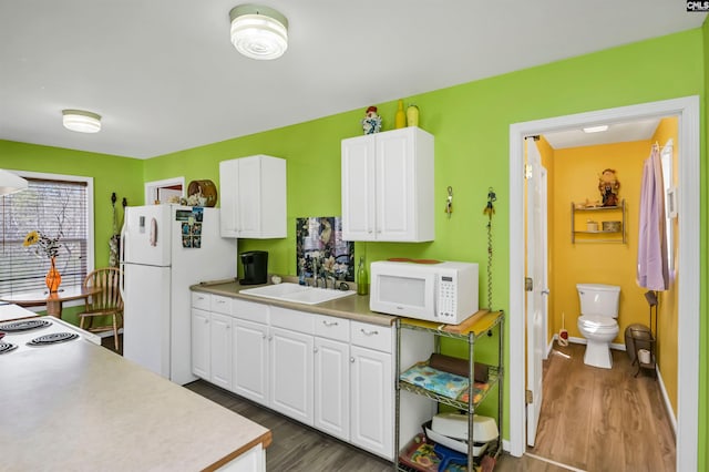 kitchen with white appliances, a sink, white cabinetry, light countertops, and dark wood-style floors