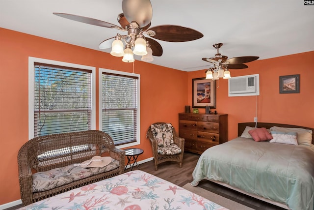 bedroom with a ceiling fan, a wall unit AC, baseboards, and wood finished floors