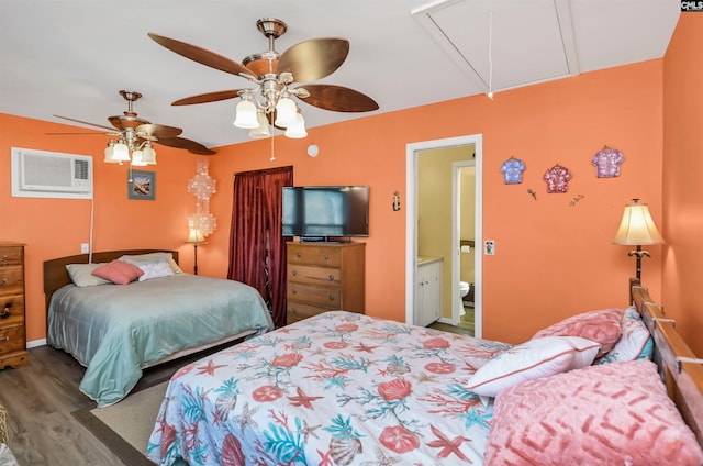 bedroom with a wall unit AC, wood finished floors, attic access, and a ceiling fan