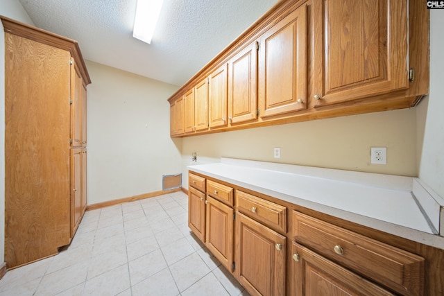 kitchen featuring baseboards, vaulted ceiling, light countertops, a textured ceiling, and light tile patterned flooring