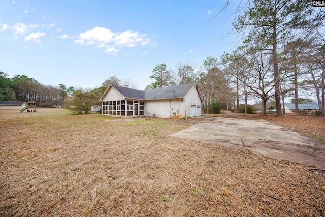 back of property with an attached garage, a sunroom, and a lawn