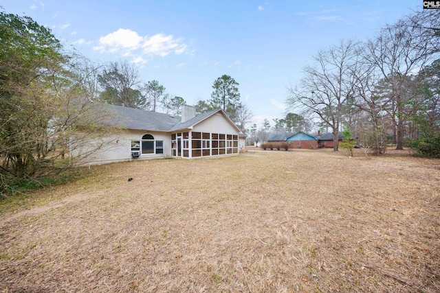 rear view of house featuring a sunroom, a chimney, and a lawn