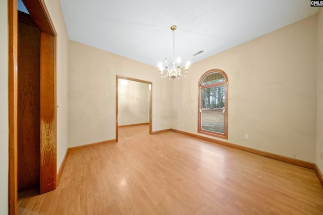 spare room featuring light wood-type flooring, an inviting chandelier, baseboards, and visible vents