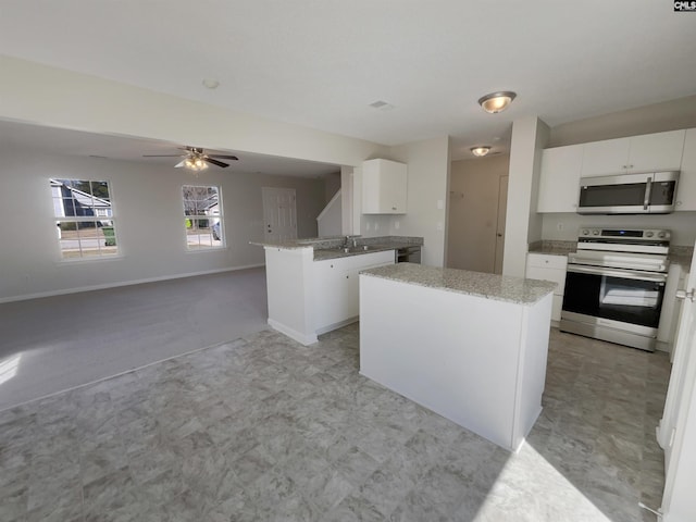 kitchen featuring baseboards, white cabinets, light stone counters, appliances with stainless steel finishes, and a sink