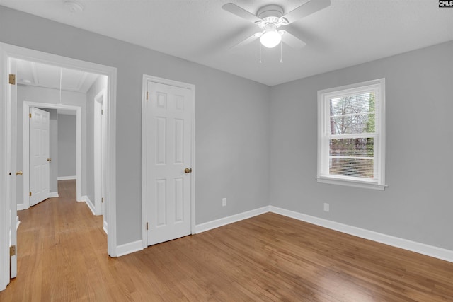 empty room with attic access, light wood-type flooring, ceiling fan, and baseboards