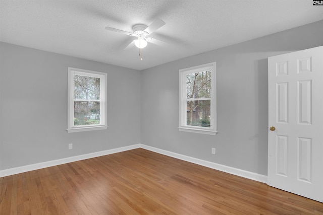 empty room with a healthy amount of sunlight, a textured ceiling, baseboards, and wood finished floors