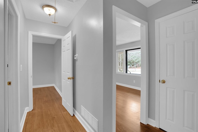 hall featuring a textured ceiling, wood finished floors, visible vents, and baseboards