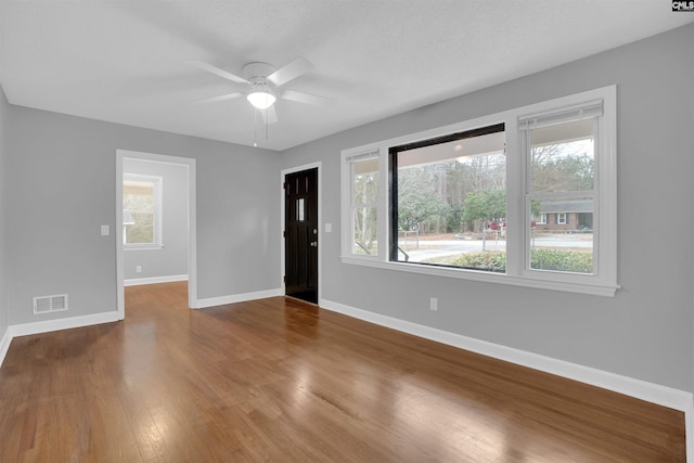 foyer entrance with a ceiling fan, visible vents, baseboards, and wood finished floors