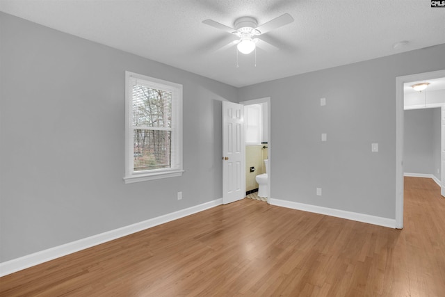 unfurnished bedroom with a textured ceiling, ceiling fan, connected bathroom, baseboards, and light wood-type flooring