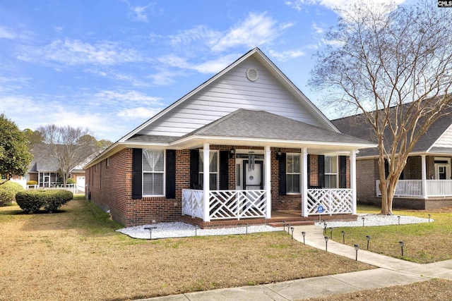 bungalow with brick siding, a porch, a shingled roof, and a front yard