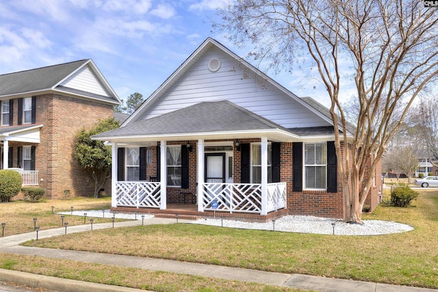 bungalow-style house featuring covered porch, roof with shingles, a front yard, and brick siding