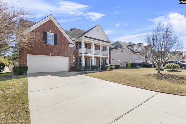 neoclassical home with a front yard, concrete driveway, brick siding, and a balcony