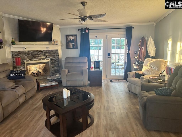 living area featuring a stone fireplace, crown molding, a textured ceiling, and wood finished floors