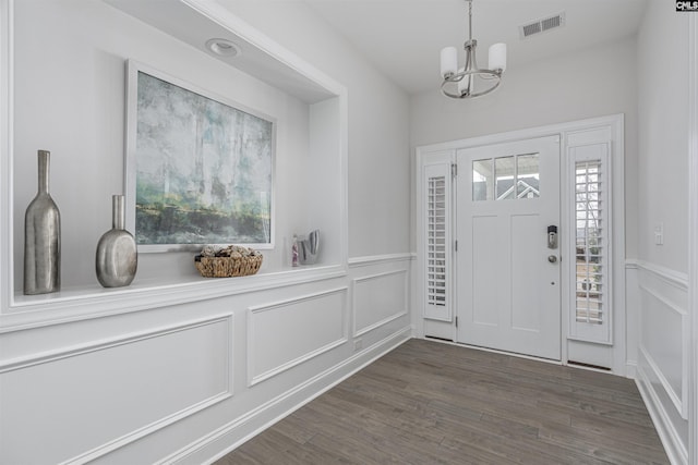 entrance foyer featuring dark wood-style flooring, a wainscoted wall, visible vents, a decorative wall, and an inviting chandelier