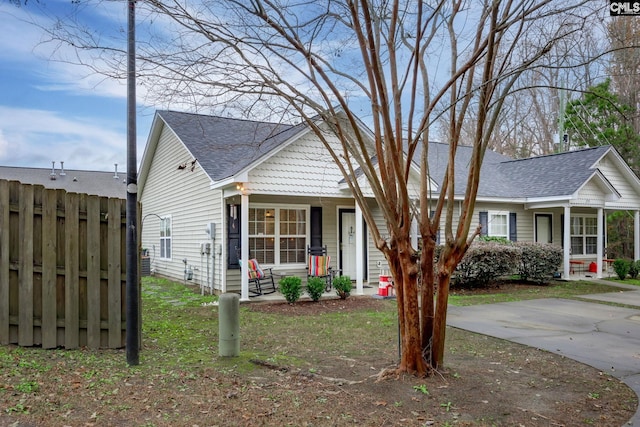 view of front facade with covered porch, a shingled roof, and fence