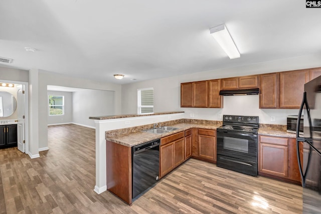 kitchen with under cabinet range hood, a peninsula, a sink, black appliances, and light wood finished floors