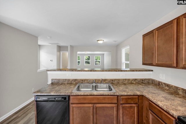 kitchen with a peninsula, wood finished floors, a sink, black appliances, and brown cabinetry