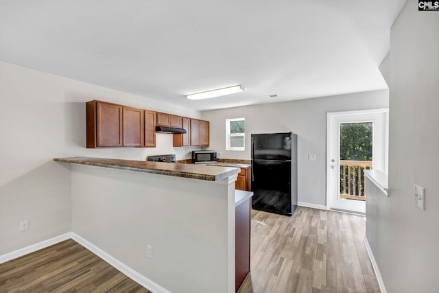 kitchen featuring under cabinet range hood, a peninsula, freestanding refrigerator, stainless steel microwave, and plenty of natural light