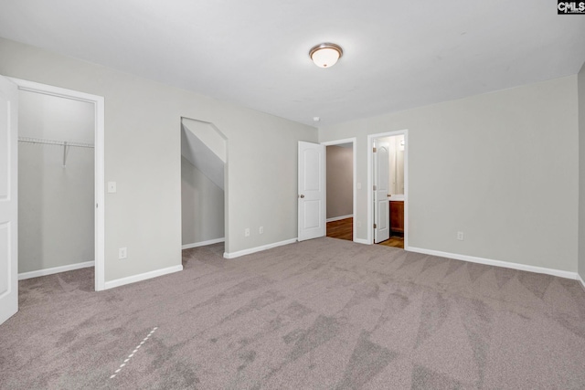 unfurnished bedroom with carpet floors, connected bathroom, a spacious closet, and baseboards